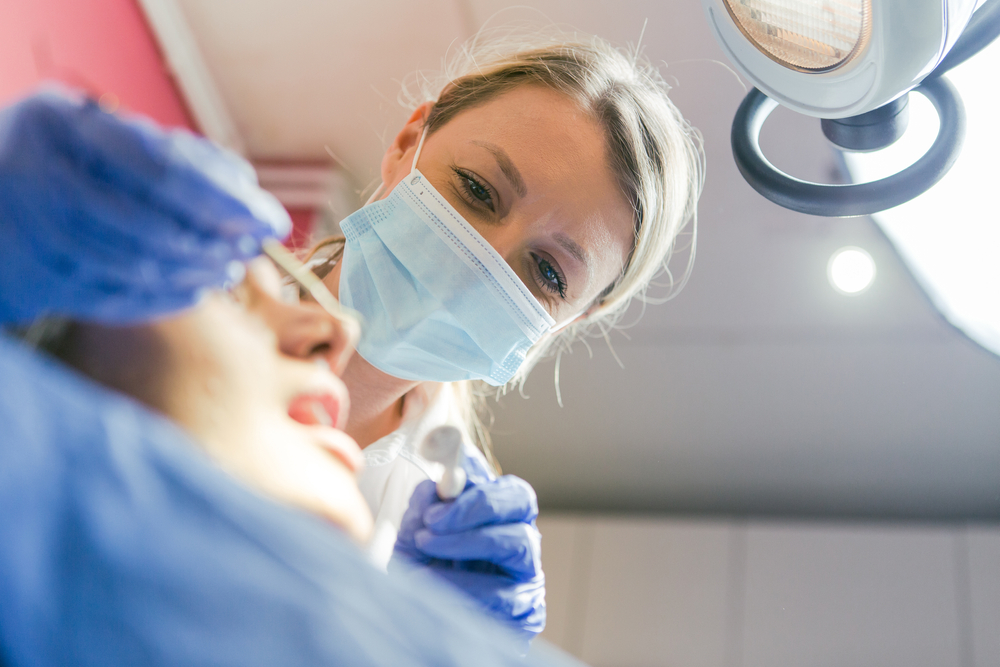 Close up shot of a dentist's hands attaching an abutment to a dental implant inside a patient's mouth. No text on image.