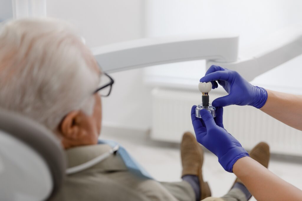 Elderly man being shown dental implant by purple gloved hands